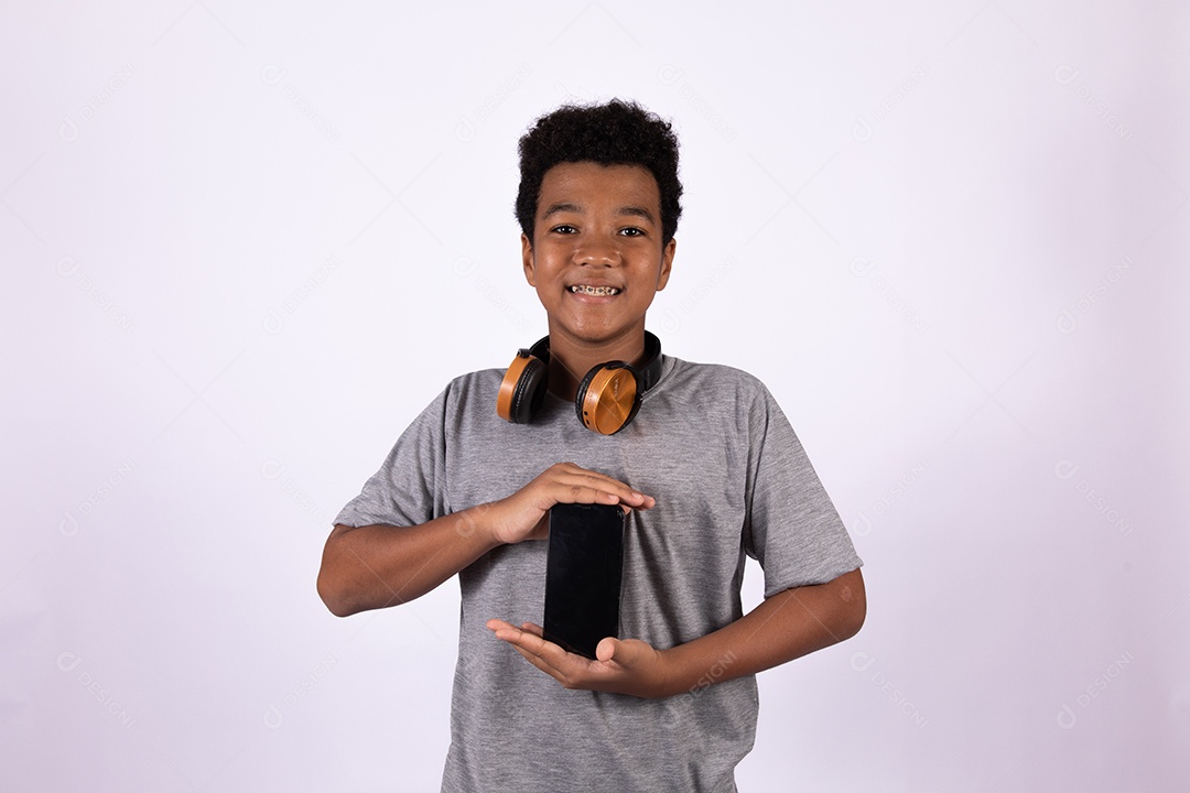 Menino jovem usando fones de ouvido segurando celular smartphone sobre fundo isolado