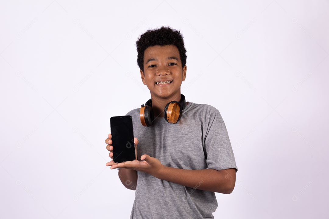 Menino jovem segurando celular smartphone usando fones de ouvido sobre fundo isolado