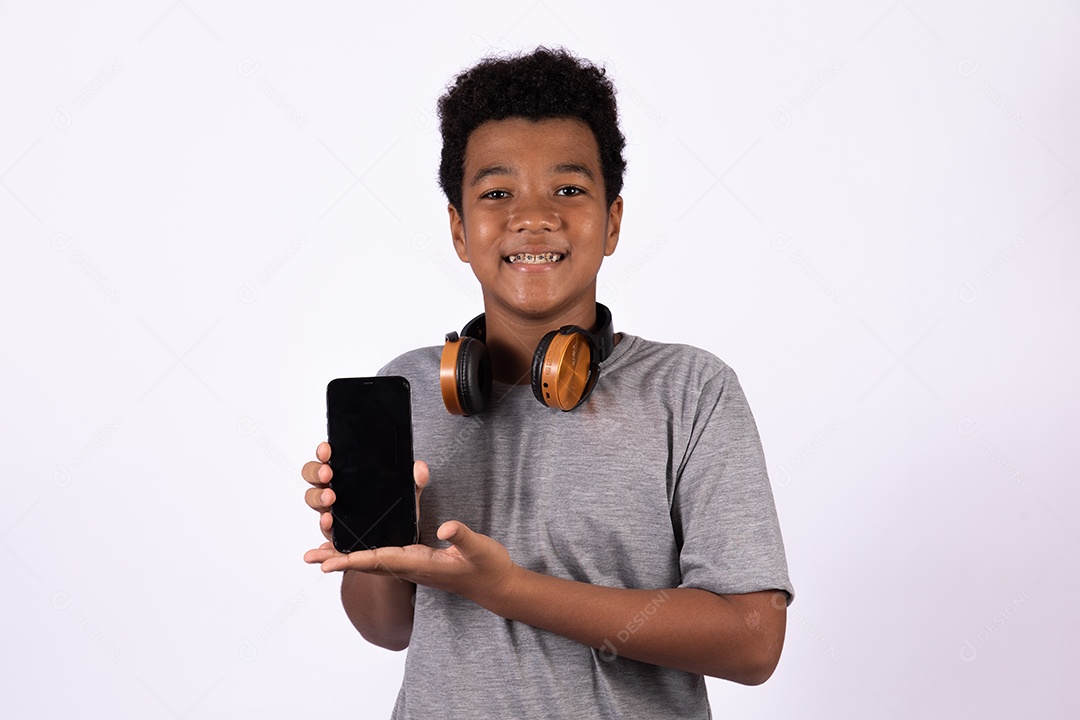 Menino jovem usando fones de ouvido segurando celular smartphone sobre fundo isolado