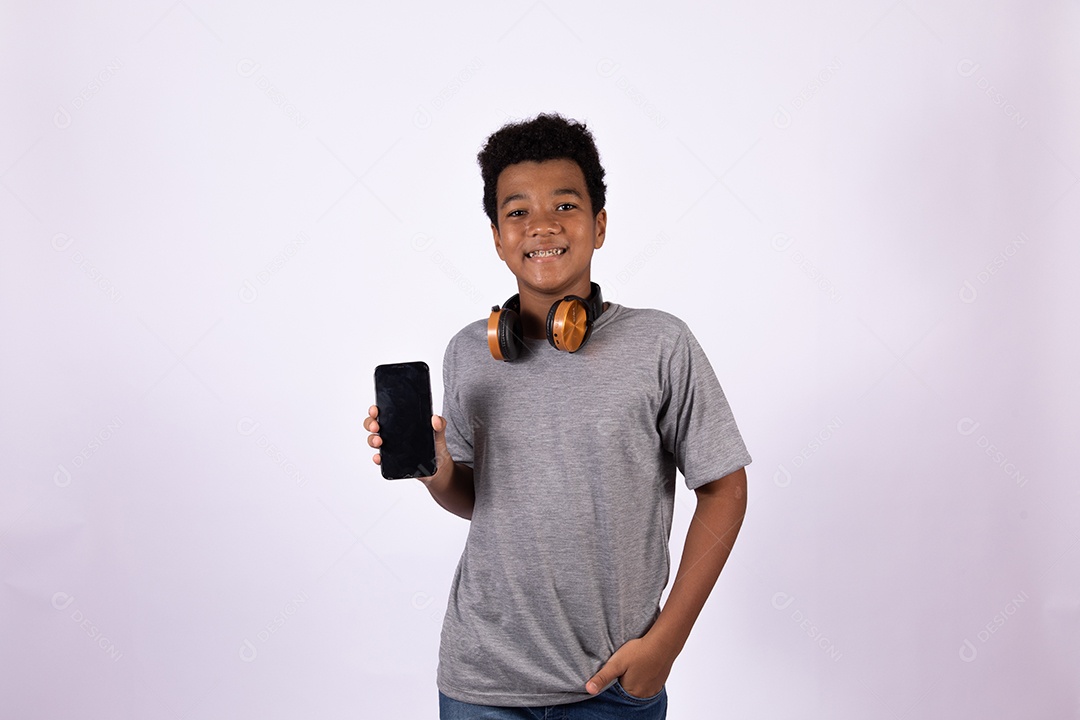 Menino jovem usando fones de ouvido segurando celular smartphone sobre fundo isolado