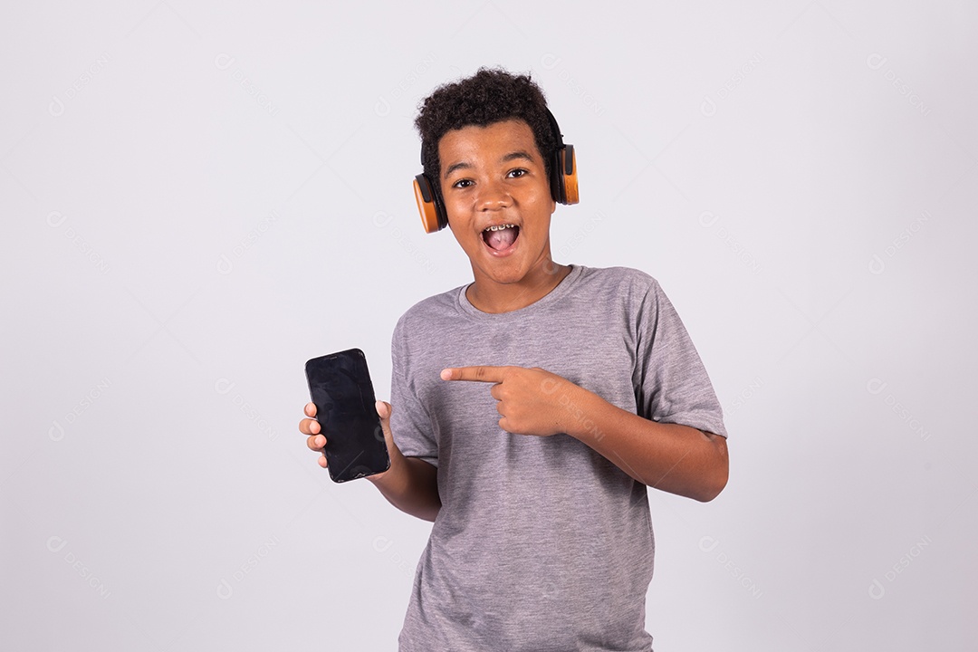 Menino jovem usando fones de ouvido segurando celular smartphone sobre fundo isolado