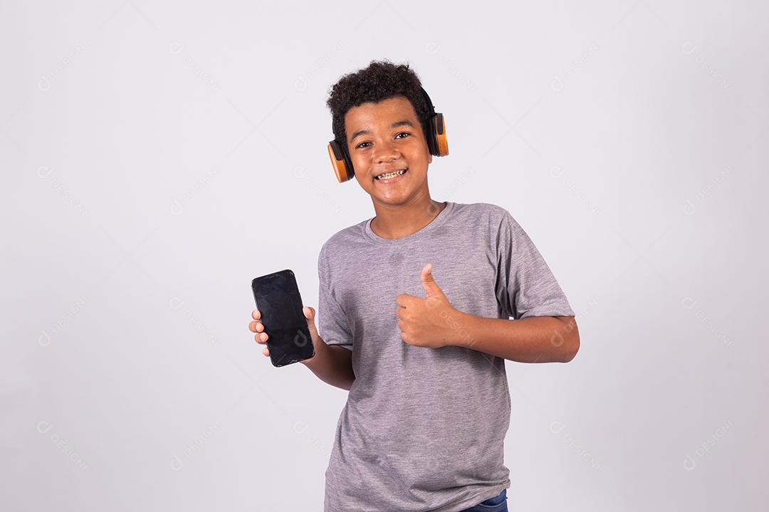 Menino jovem usando fones de ouvido segurando celular smartphone sobre fundo isolado