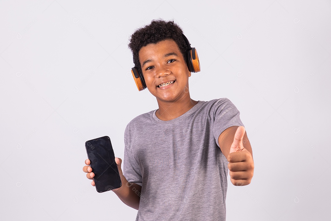 Menino jovem usando fones de ouvido segurando celular smartphone sobre fundo isolado