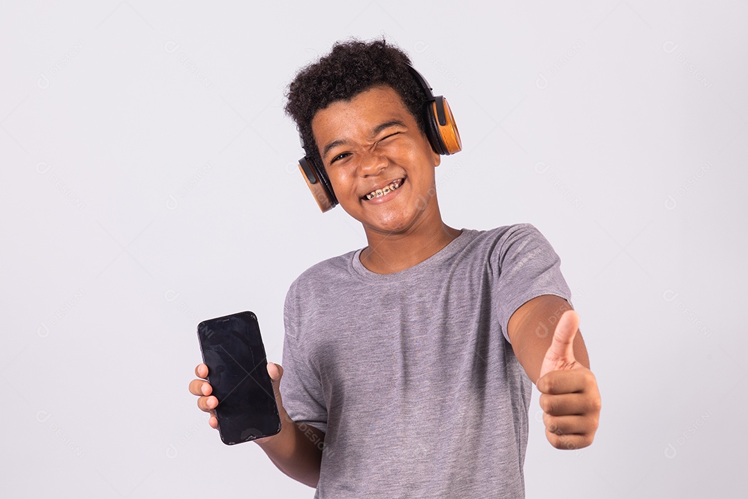 Menino jovem usando fones de ouvido segurando celular smartphone sobre fundo isolado