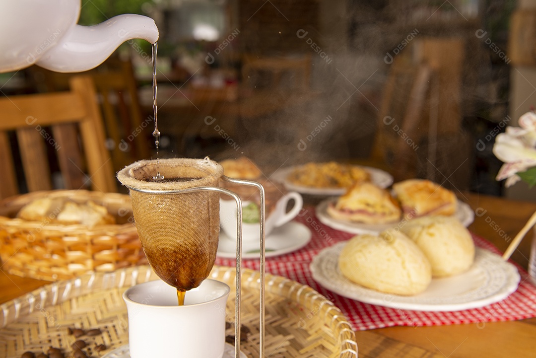 Café coado direto na xícara sobre uma mesa com pão de queijo.