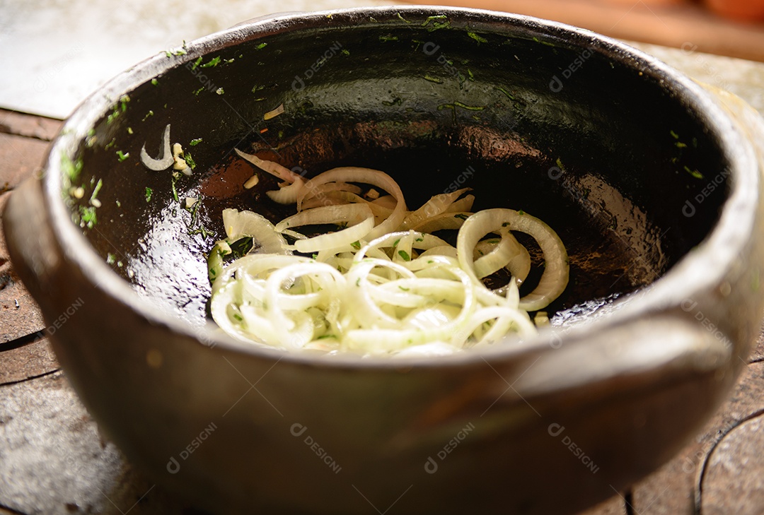 Cebola fatiada sendo refogada em panela de barro