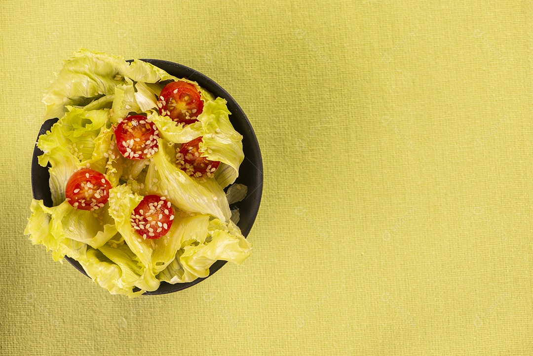 Tigela preta com salada de alface e tomate cereja e gergelim branco