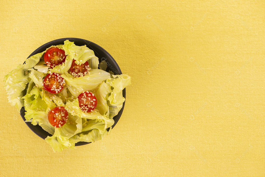 Tigela preta com salada de alface e tomate cereja e gergelim branco