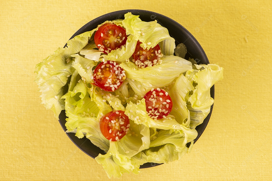 Tigela preta com salada de alface e tomate cereja e gergelim branco