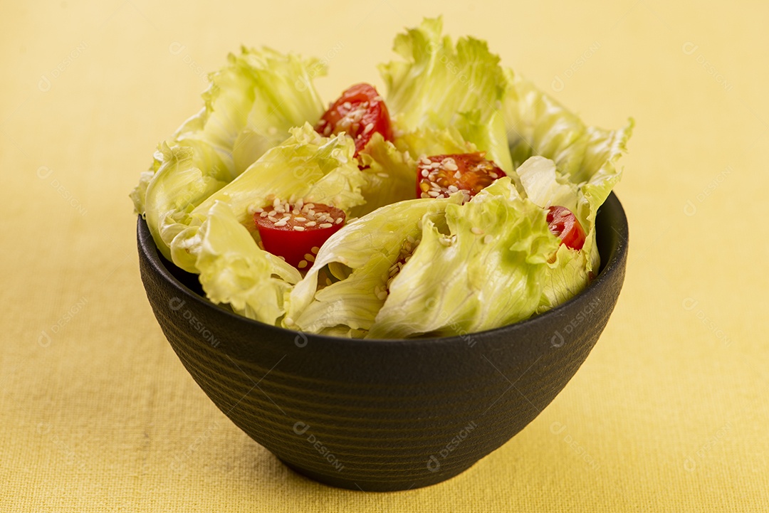 Tigela preta com salada de alface e tomate cereja e gergelim branco