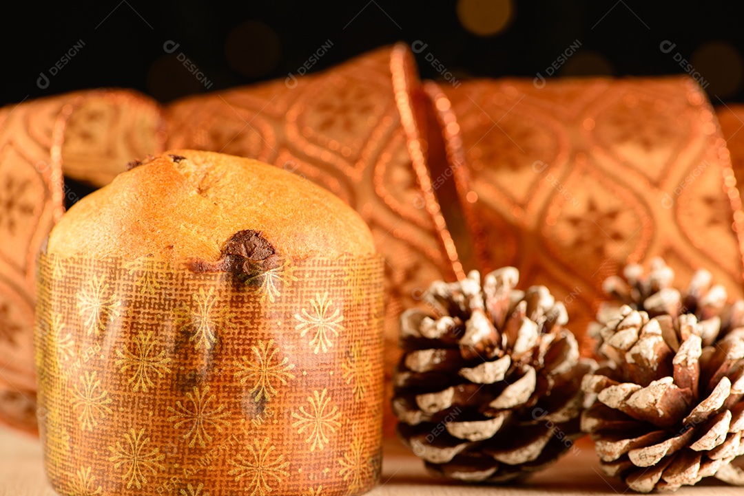 Pequeno panetone ao lado de pinhas e fita decorativa