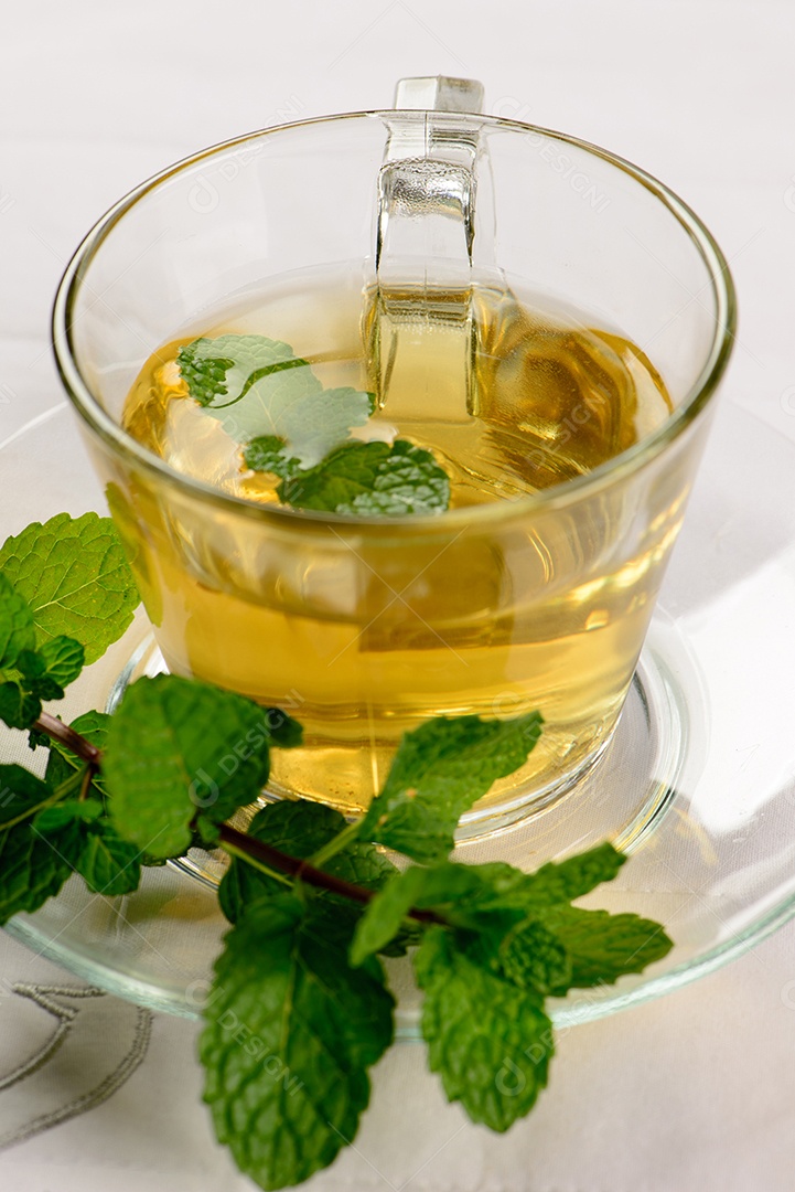 Chá de menta em copo transparente com raminho de menta ao lado