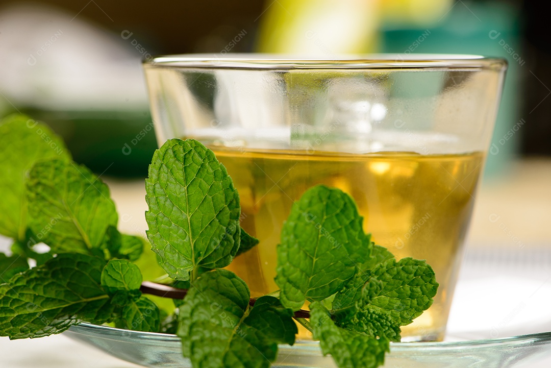 Chá de menta em copo transparente com raminho de menta ao lado