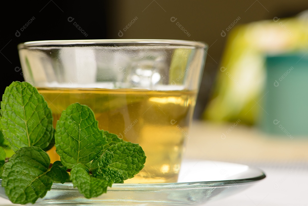 Chá de menta em copo transparente com raminho de menta ao lado