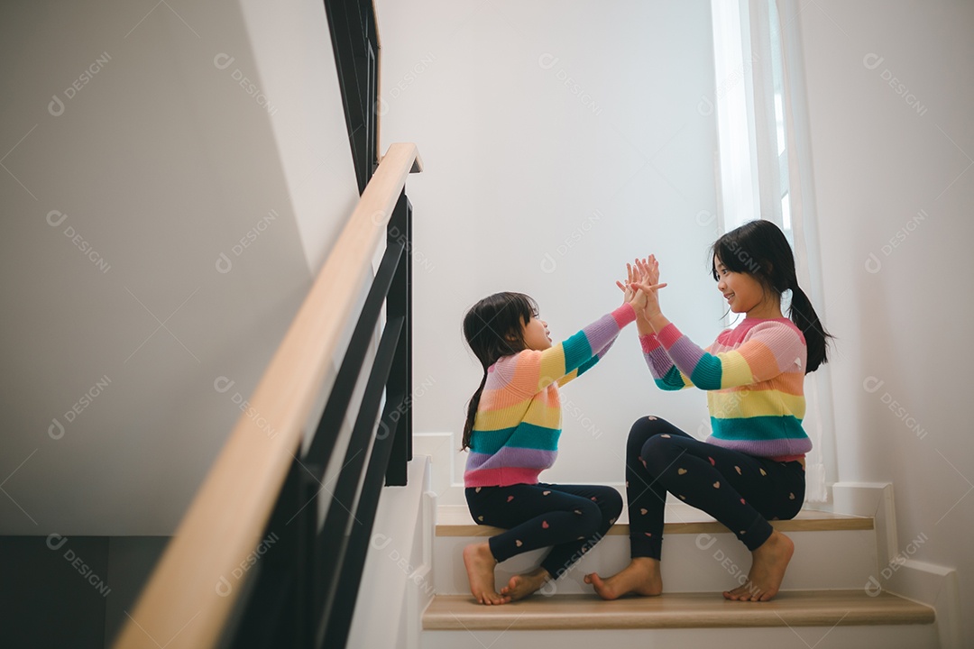 Meninas asiáticas irmãs jogando pedra, papel, tesoura, jogo de mão. crianças sentadas na escada em casa brincando juntas.