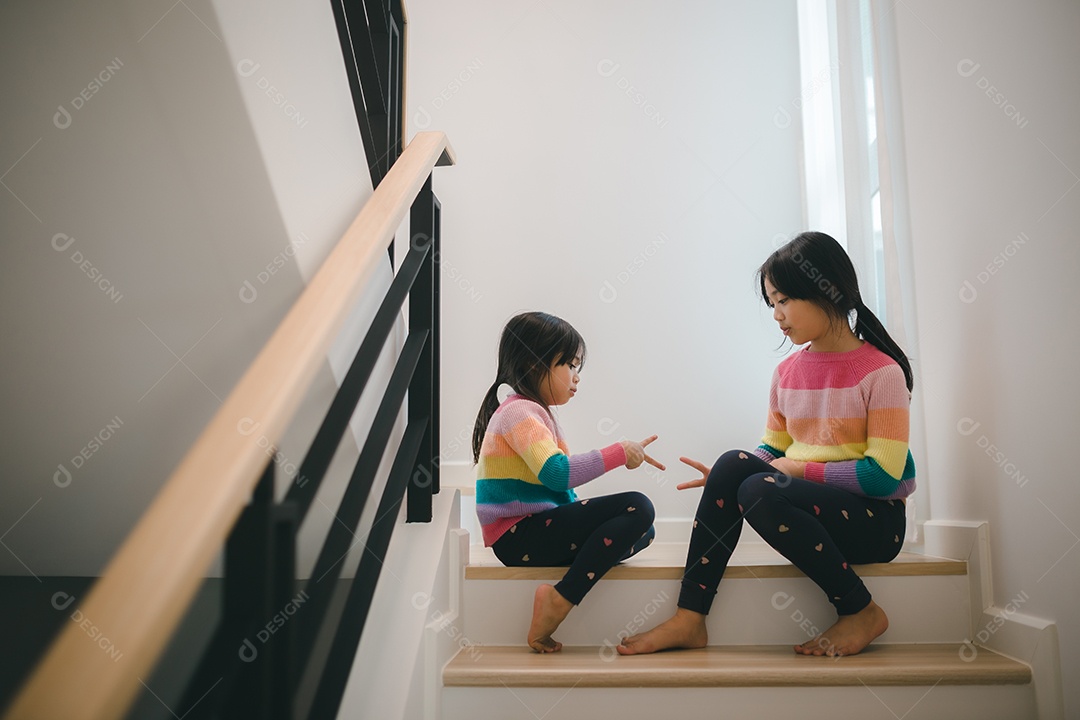 Meninas asiáticas irmãs jogando pedra, papel, tesoura, jogo de mão. crianças sentadas na escada em casa brincando juntas.