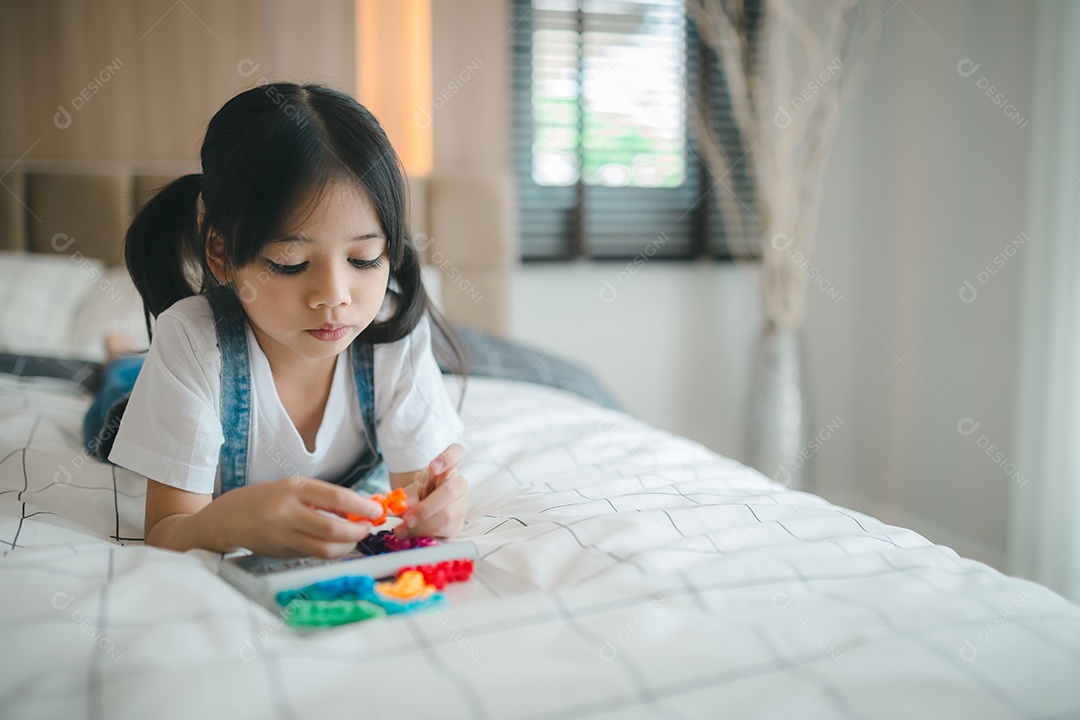 Criança asiática brincando com brinquedos na cama no quarto.