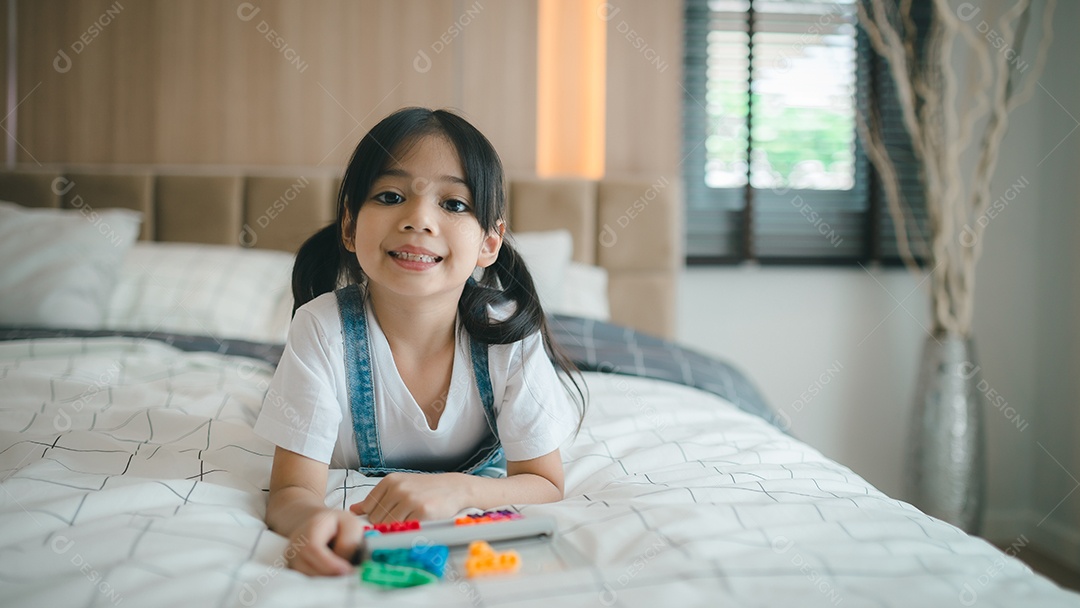 Criança asiática brincando com brinquedos na cama no quarto.