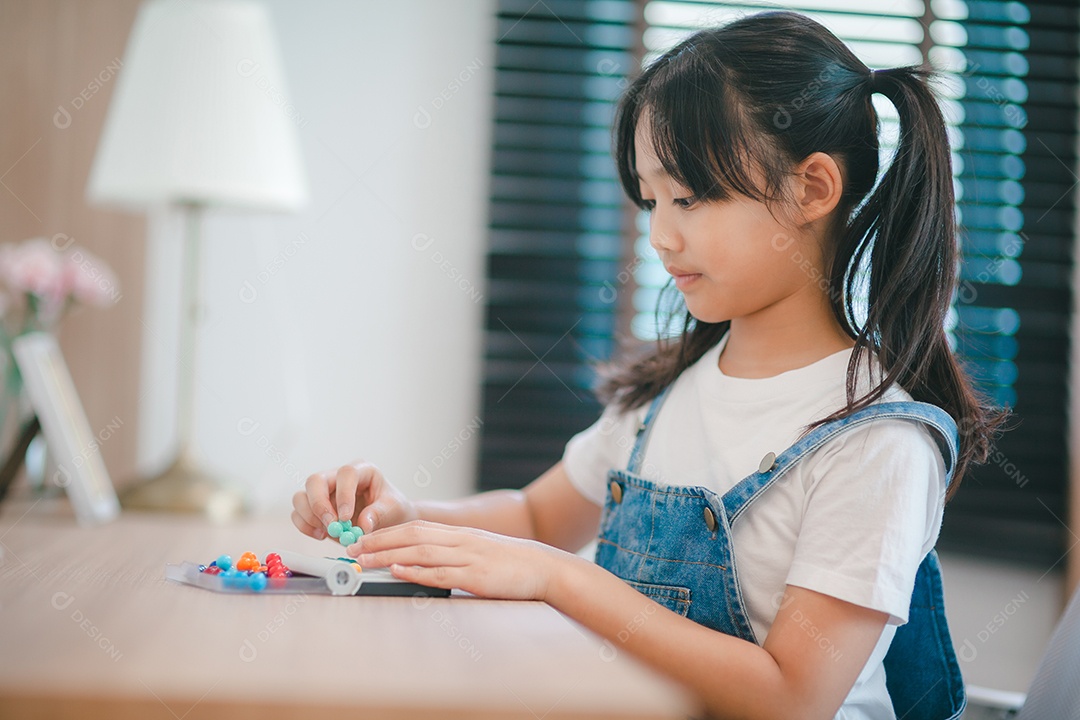 Menina asiática bonitinha curtindo enquanto brincava com brinquedos ou blocos, sentada à mesa.