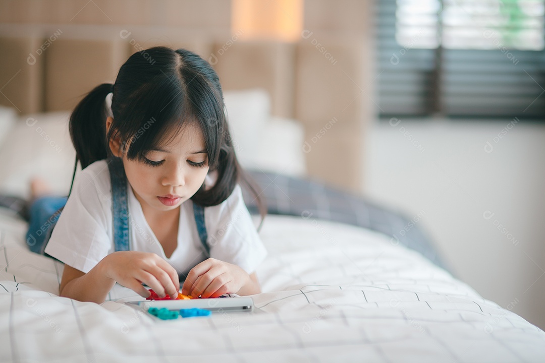 Menina asiática bonitinha curtindo enquanto brincava com brinquedos ou blocos, sentada à mesa.