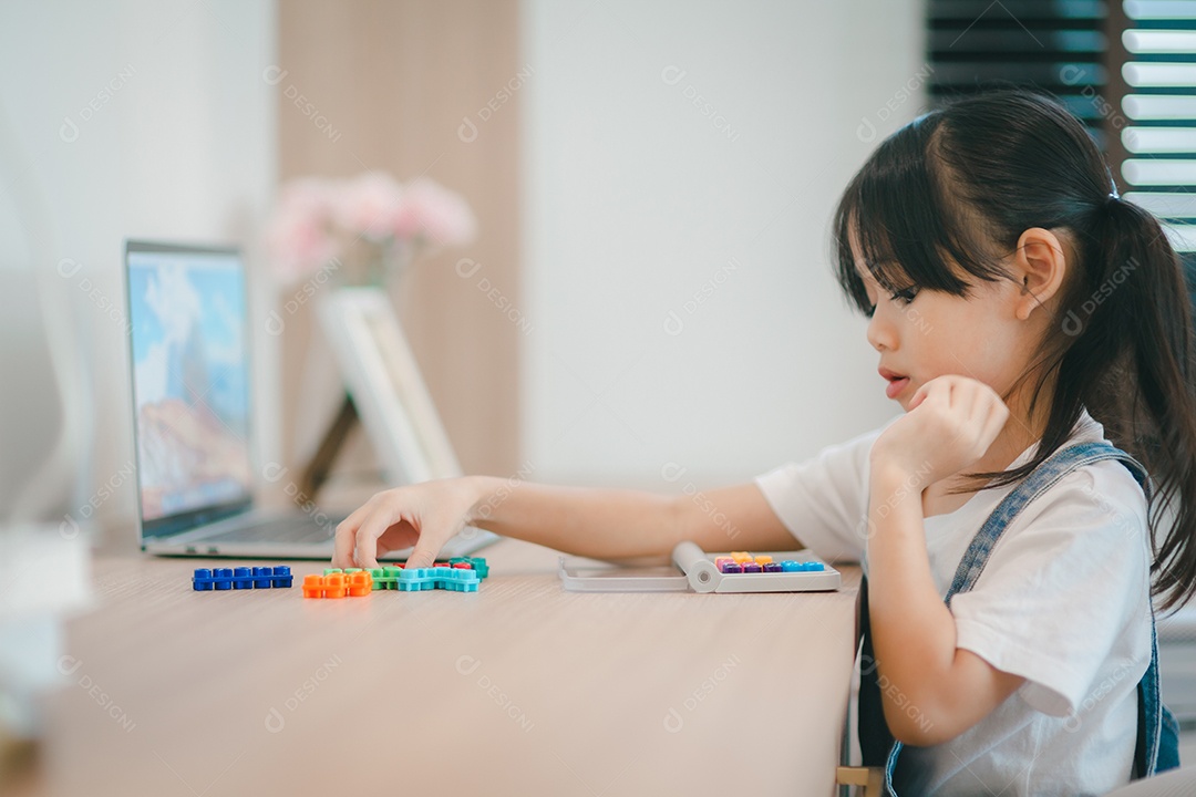 Menina asiática bonitinha curtindo enquanto brincava com brinquedos ou blocos, sentada à mesa.