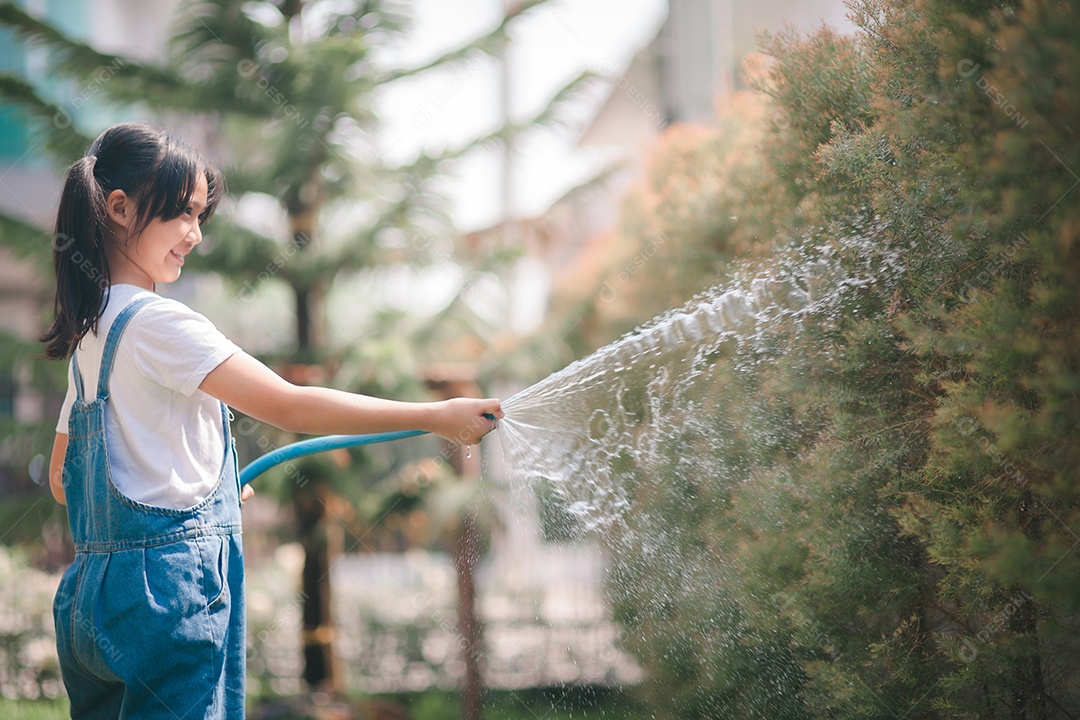 A menina asiática da criança rega as plantas. garoto ajuda a cuidar das plantas do jardim.