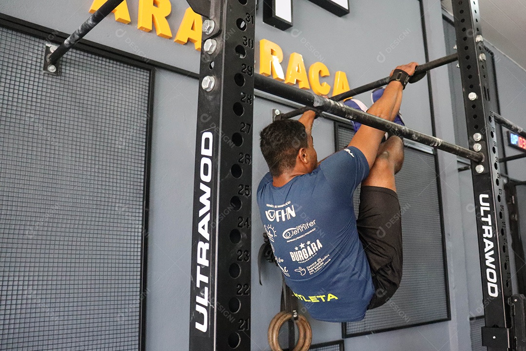 Belo homem moreno fazendo exercício em barra sobre uma academia
