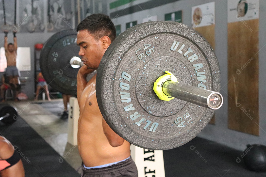 Belo homem moreno fazendo levantamento de peso sobre uma academia