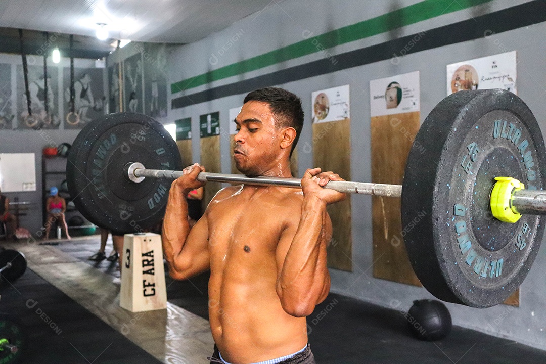 Belo homem moreno fazendo levantamento de peso sobre uma academia