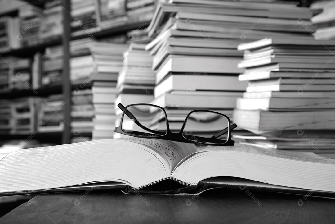 Livros sobre a mesa e estantes ao fundo