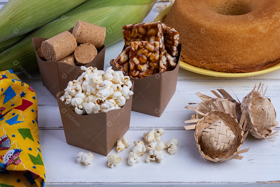 Milho verde e doces da festa junina na mesa de madeira branca.