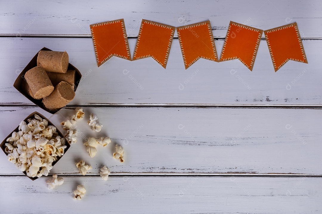 Tigelas de pipoca e doces de amendoim e bandeiras de papel em uma mesa de madeira branca.