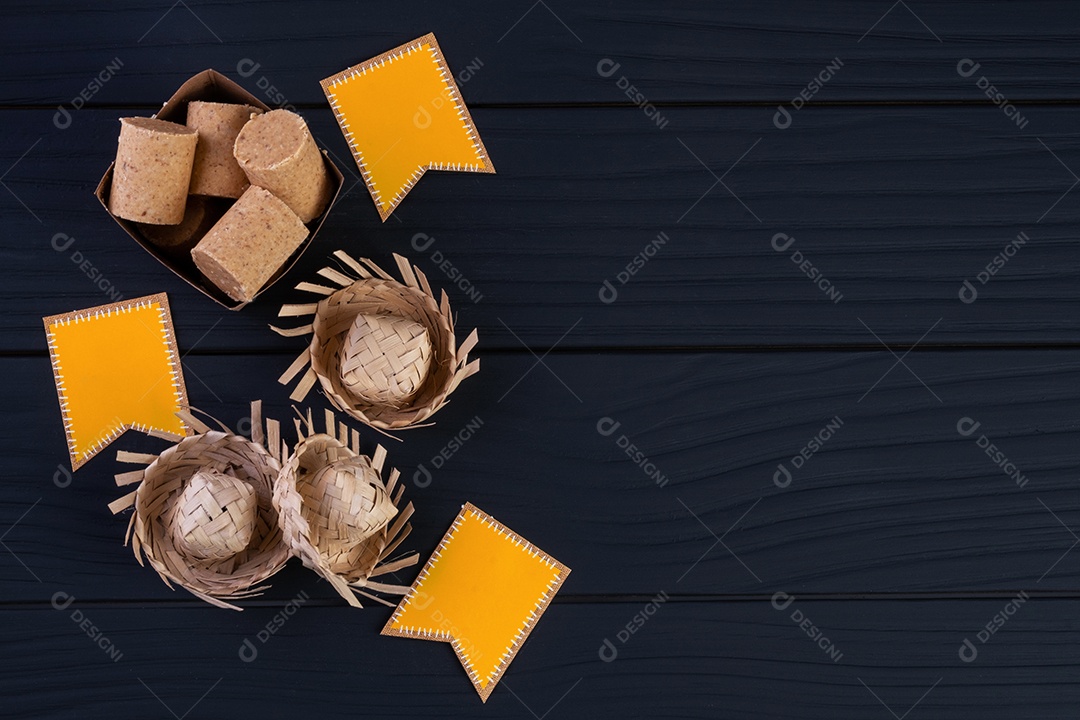 Decorações e alimentos de festa junina na mesa de madeira preta.