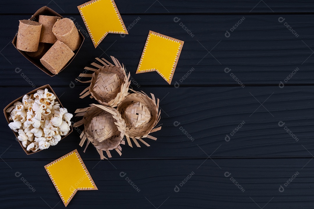 Decorações e alimentos da festa junina na mesa de madeira preta.