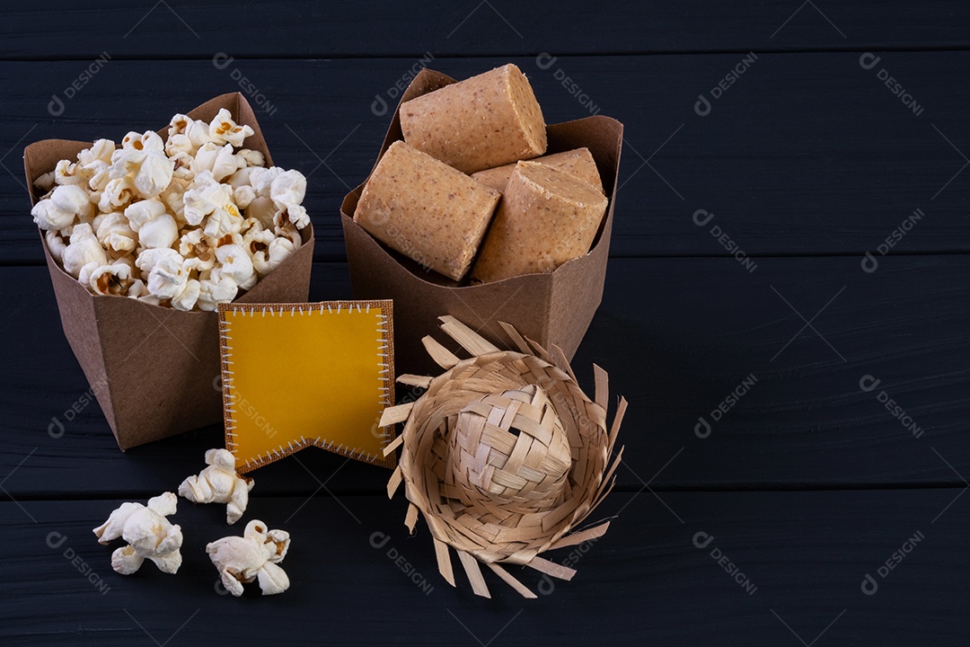 Decorações e alimentos da festa junina na mesa de madeira preta.