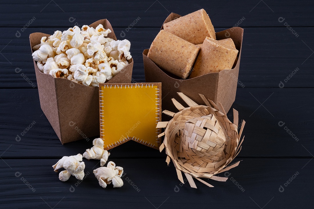 Decorações e alimentos da festa junina na mesa de madeira preta.