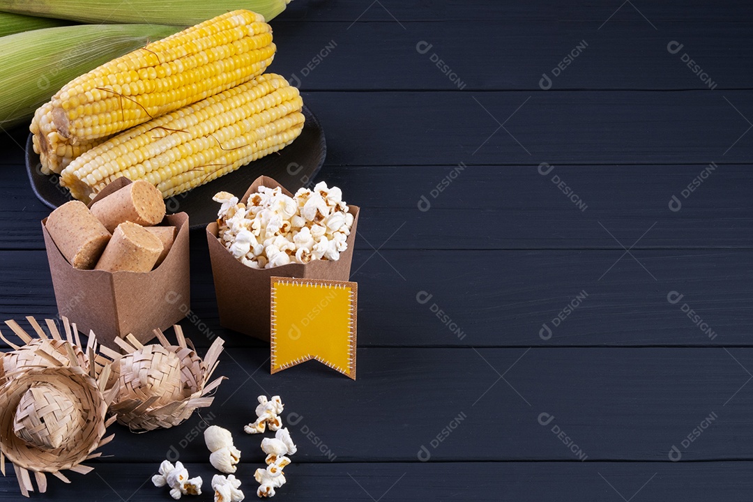 Decorações e alimentos da festa junina na mesa de madeira preta.