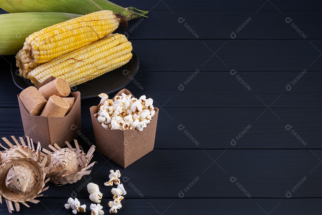 Decorações e alimentos da festa junina na mesa de madeira preta.