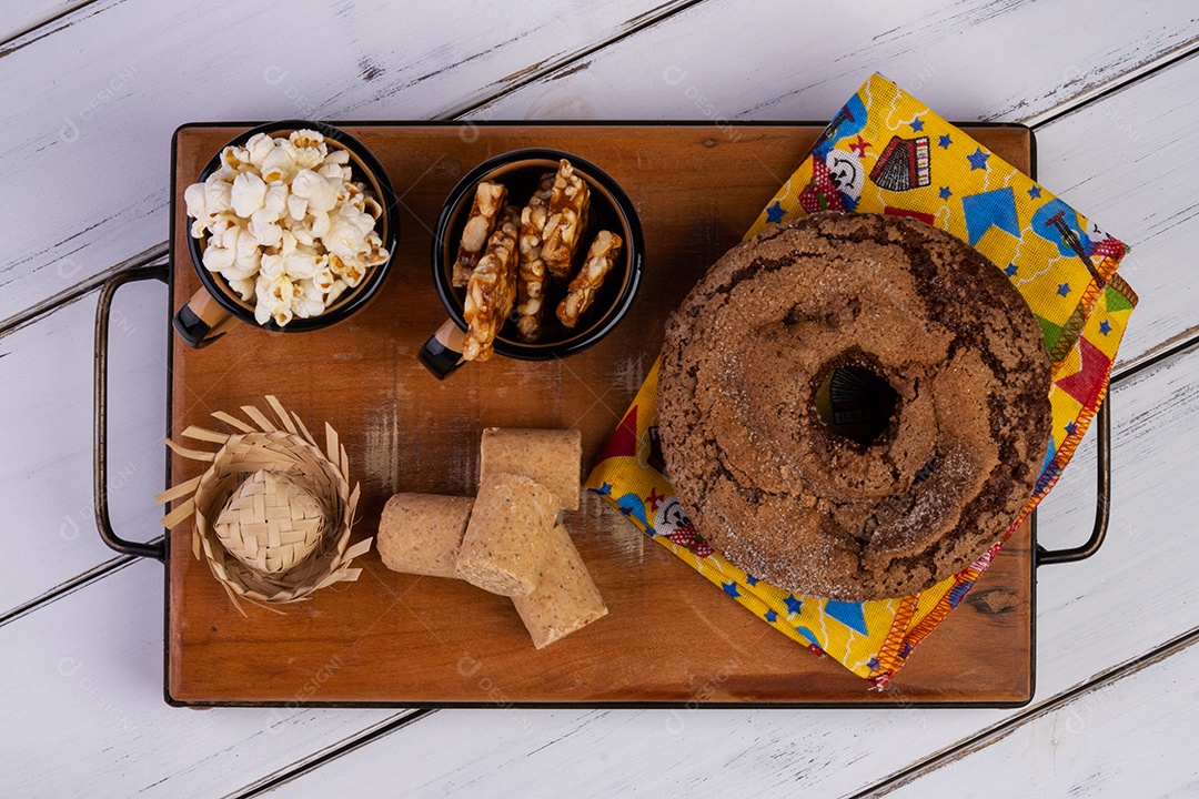 Bandeja de madeira com bolo, pipoca e docinhos de festa junina.