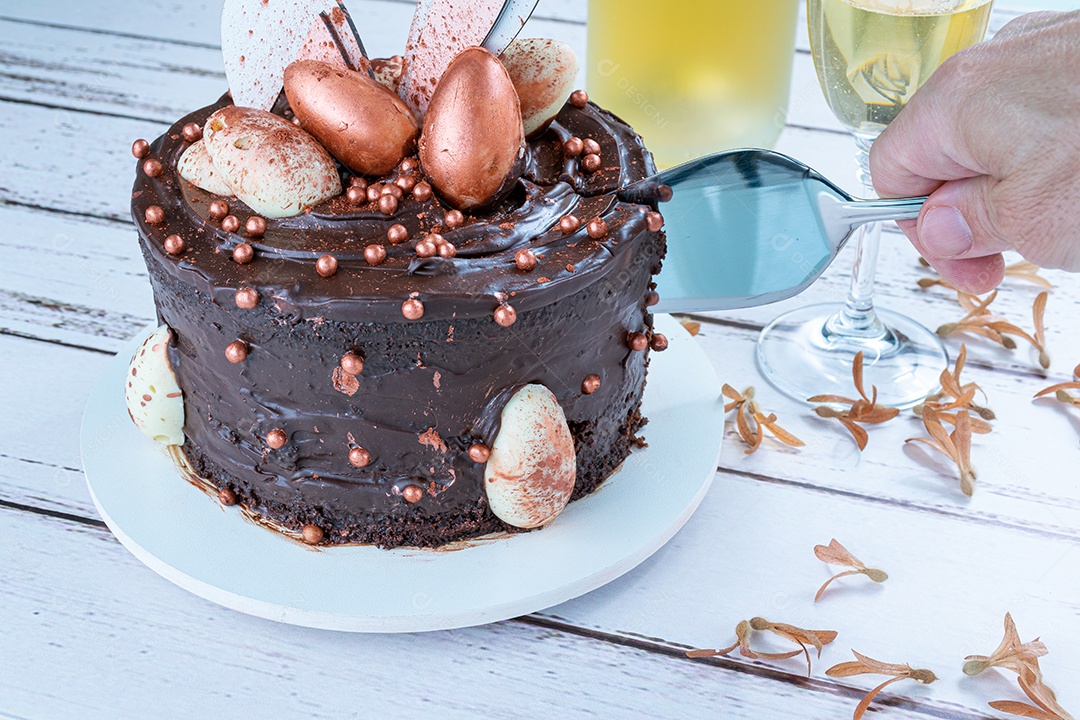 Mão masculina cortando com uma espátula o bolo de chocolate decorado com ovos de páscoa