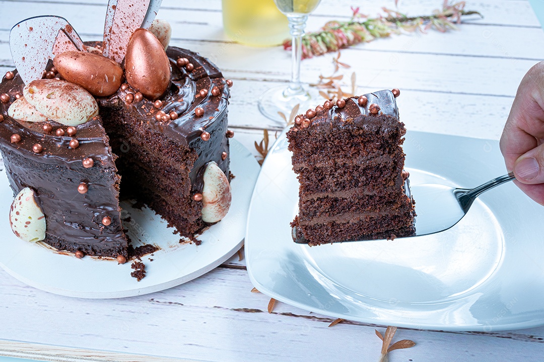 Mão masculina colocando uma fatia de bolo de chocolate decorado com ovos de páscoa