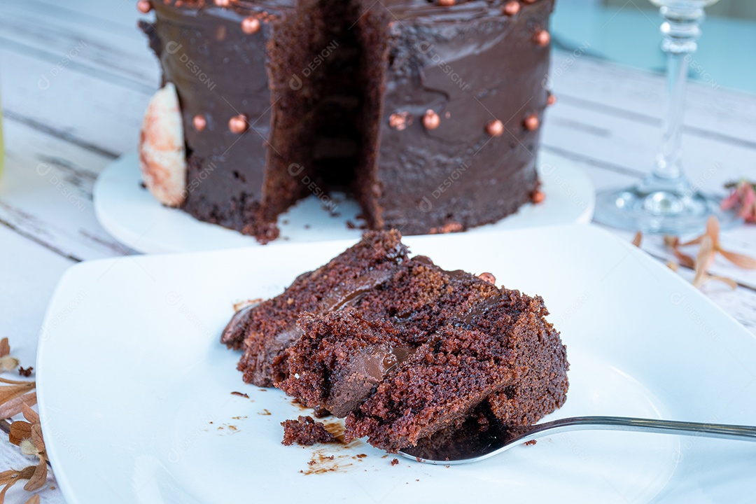 Fatia de bolo de chocolate com recheio de ganache escuro ao lado de um garfo.