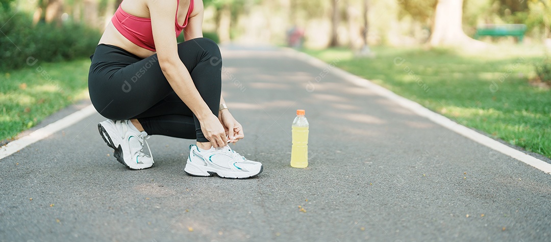 Mulher jovem atleta amarrando tênis com água Energy Drink