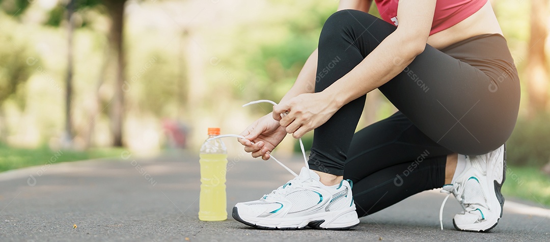 Mulher jovem atleta amarrando tênis com água Energy Drink