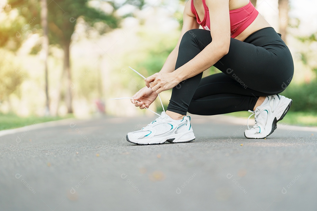 Mulher jovem atleta amarrando tênis no parque ao ar livre