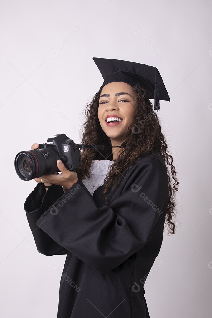 Linda mulher garota jovem segurando câmera fotográfica usando beca de formatura sobre fundo isolado