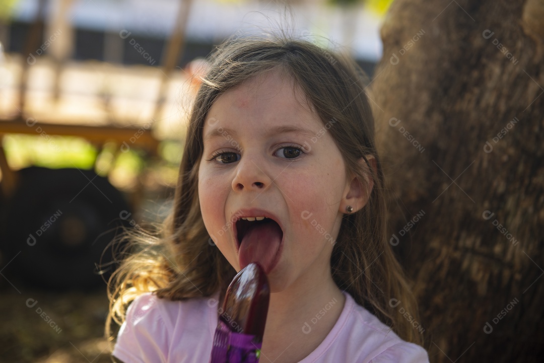 Linda garotinha comendo um sorvete de uva no palito