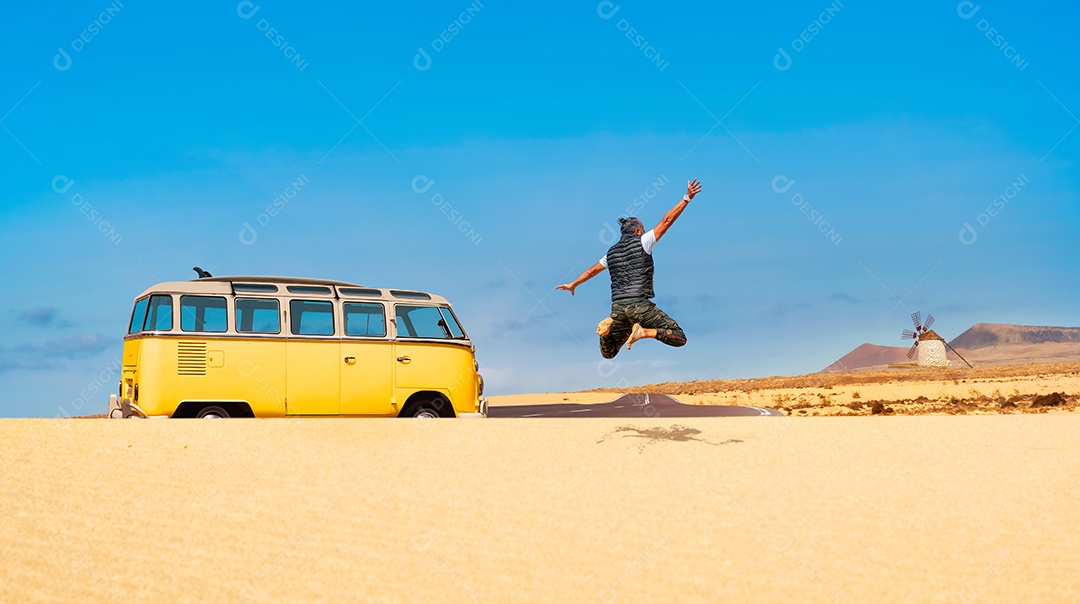 Hipster Surfer pula em dunas de areia e aprecia a paisagem do deserto - Digital Nomad viaja acampando em uma campervan vintage amarela na ilha de Fuerteventura