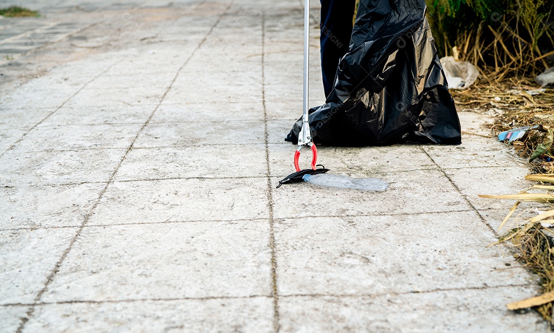 Voluntário coletando máscara facial médica usada perto de garrafa de plástico em saco plástico de lixo para limpeza de rua urbana