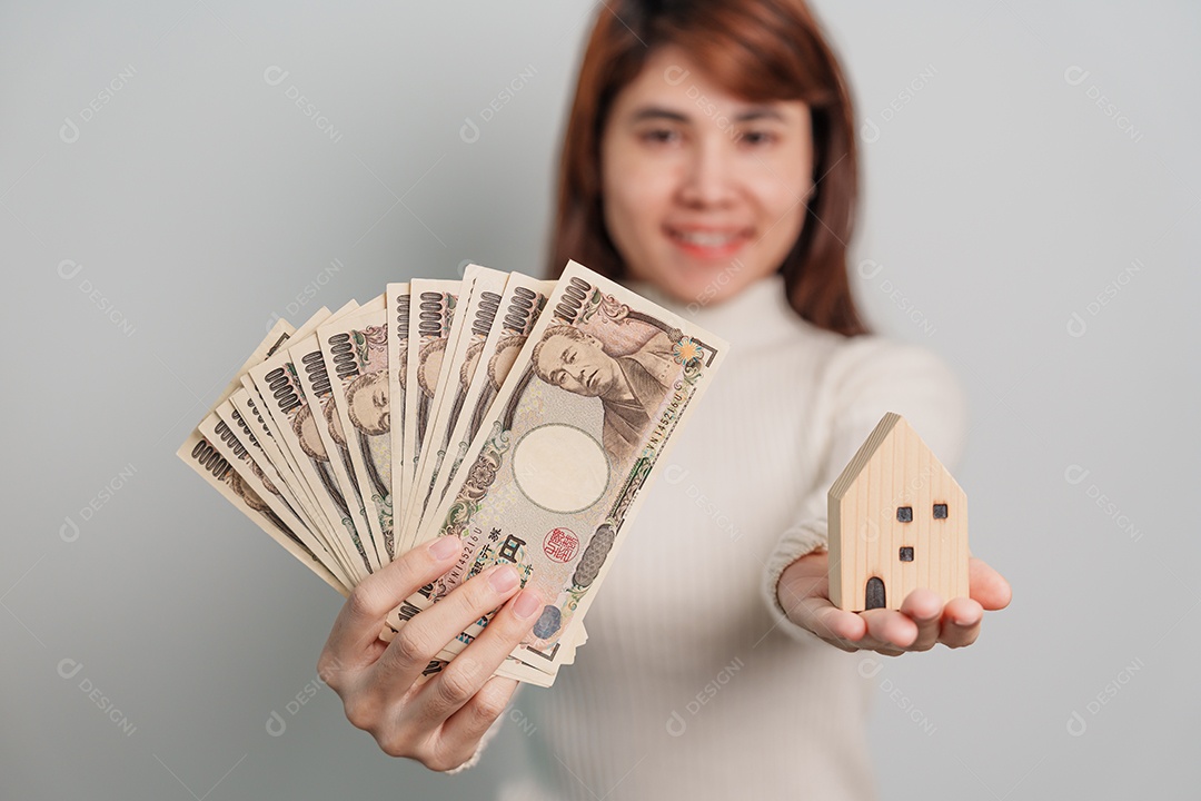 Mulher segurando notas de ienes japoneses e modelo de casa.